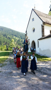 Sullo sfondo l'entrata della chiesetta di Versciaco durante la sfilata delle donne del paese in abito da festa mentre trasportano a spalla la statua della Santa 